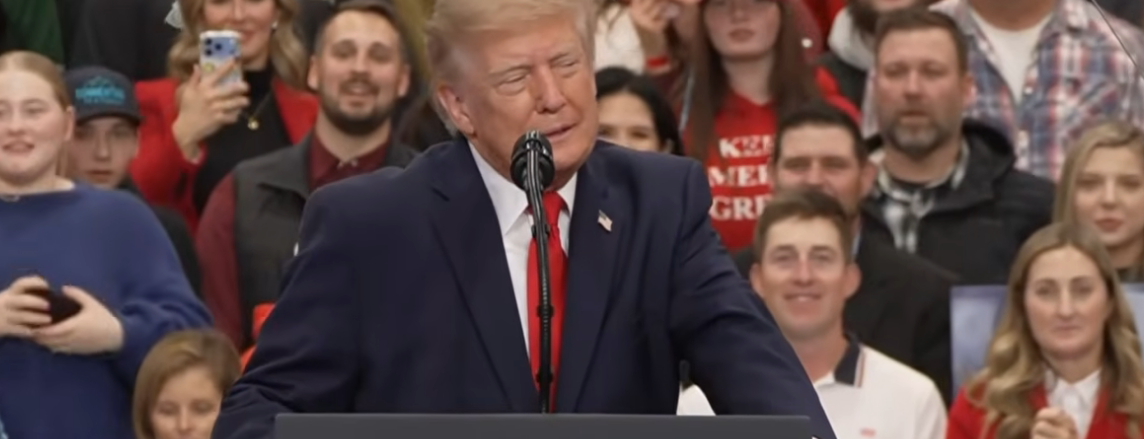 Donald Trump speaking at a political rally behind a podium with a microphone.